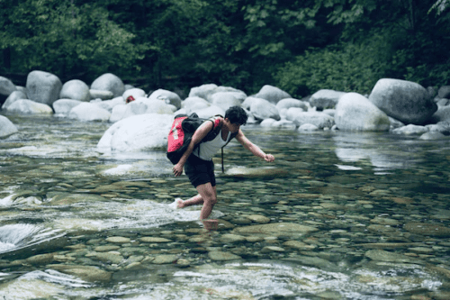 A solo hiker crossing a stream.